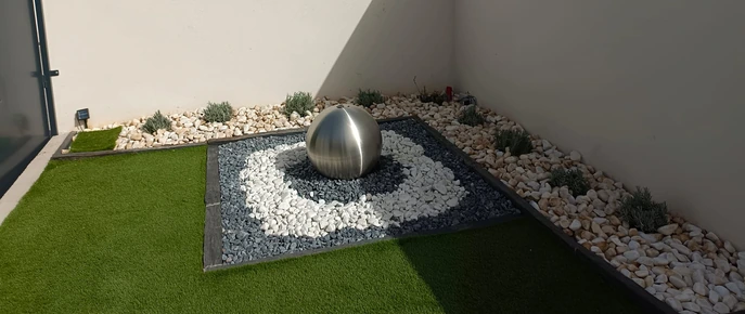 Composición de piedras blancas y grises con esfera decorativa junto al césped