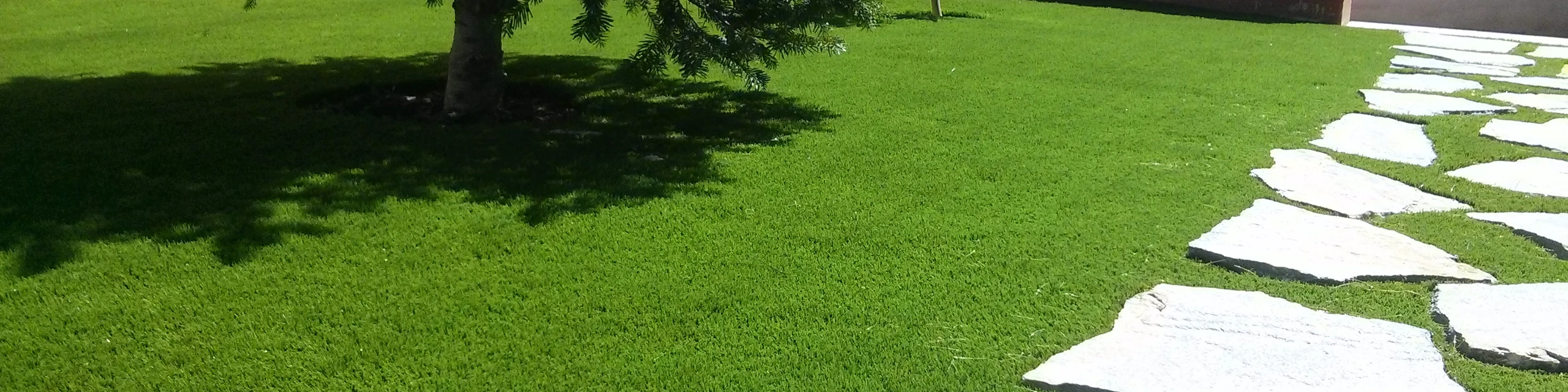 Jardín de césped artificial con un camino de losas de piedra
