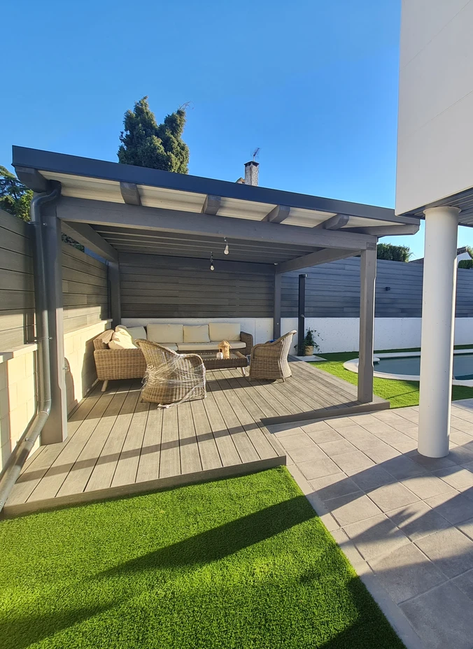 Césped artificial junto a una terraza cubierta con mobiliario exterior