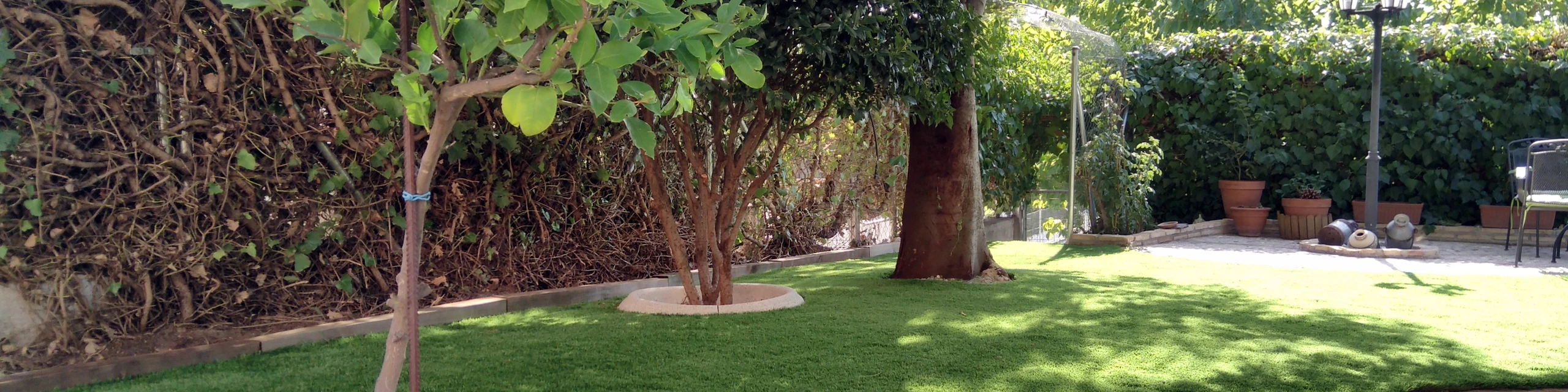 Jardín con césped artificial y árboles junto a un muro