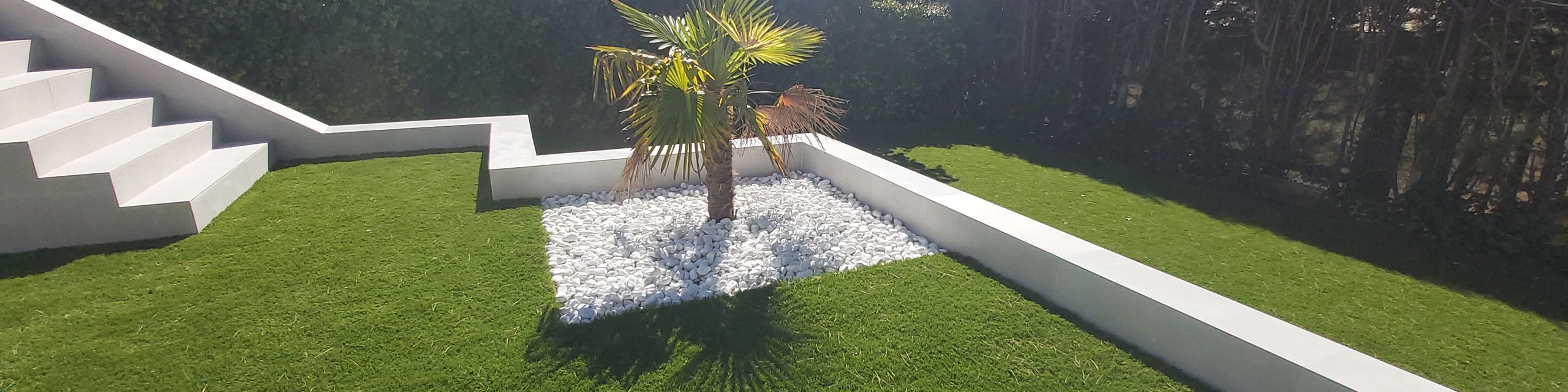 Jardín con césped artificial, escalera blanca y parterre de grava