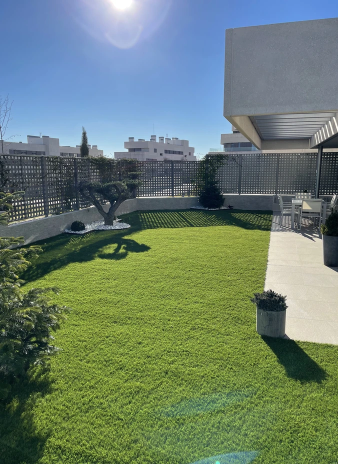 Terraza soleada con césped artificial junto a un edificio