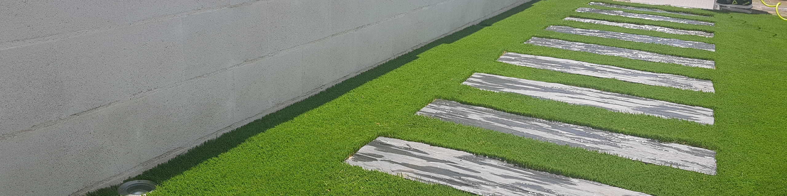 Pasos alargados de piedra sobre césped junto a un muro