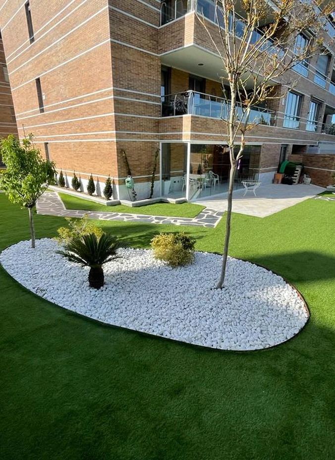 Césped artificial con un parterre de grava blanca junto a un edificio