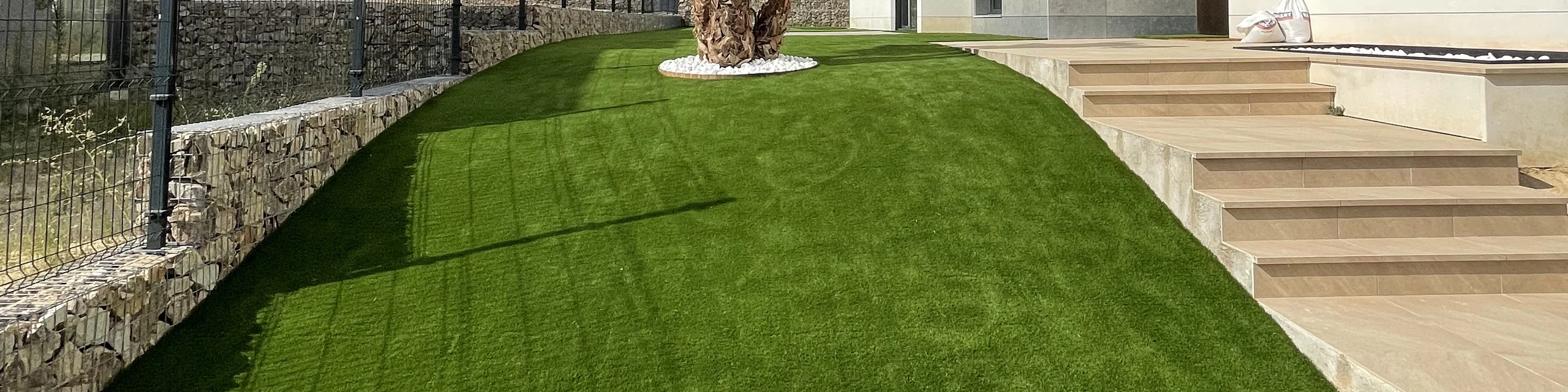 Jardín con césped artificial junto a una vivienda y escaleras