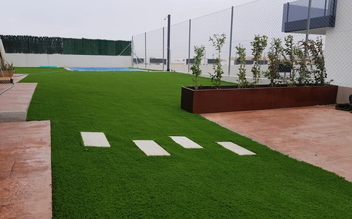 Losetas separadas sobre césped junto a una jardinera