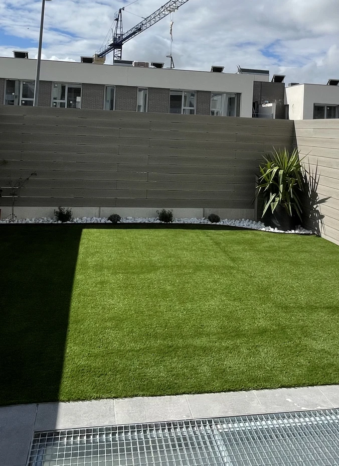 Jardín con césped artificial y grava junto a una valla