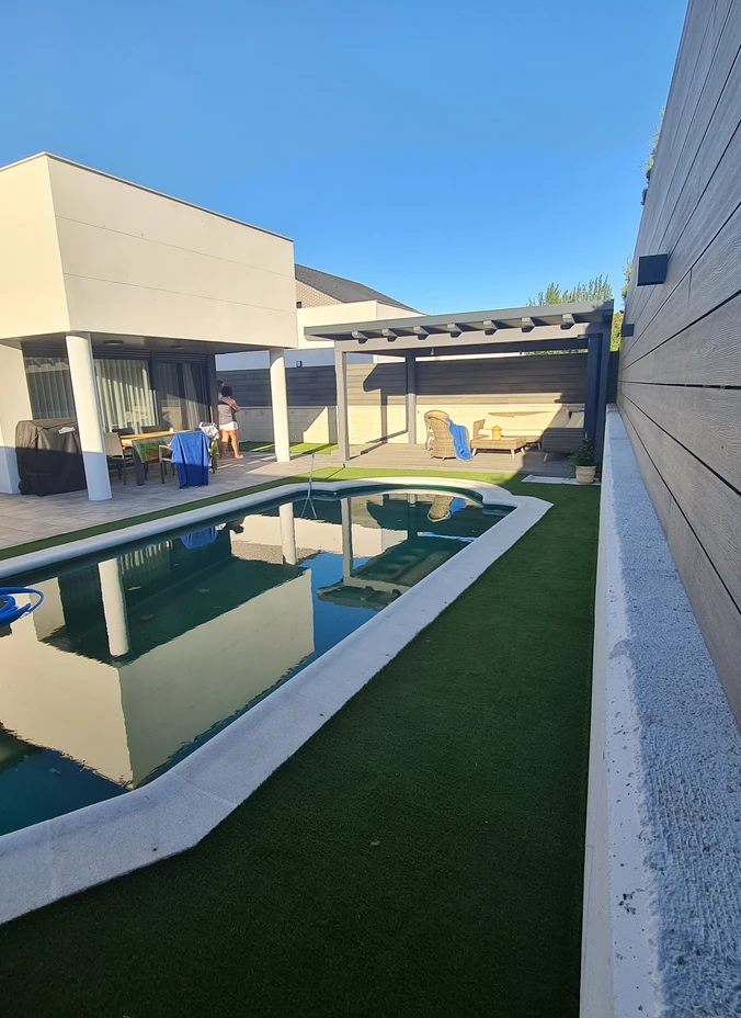 Pasillo de césped artificial junto a una piscina y una vivienda