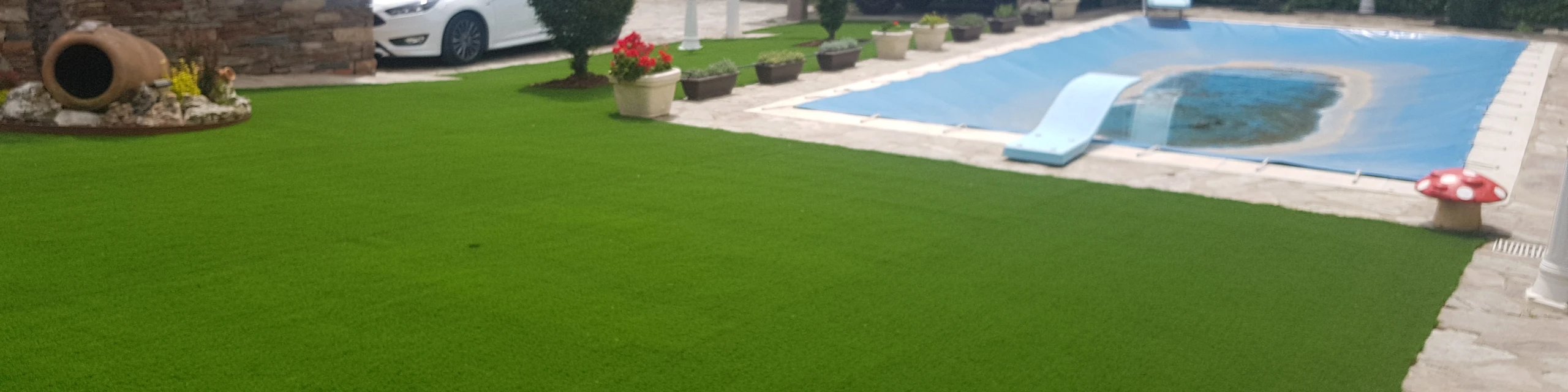 Jardín con césped artificial junto a una piscina