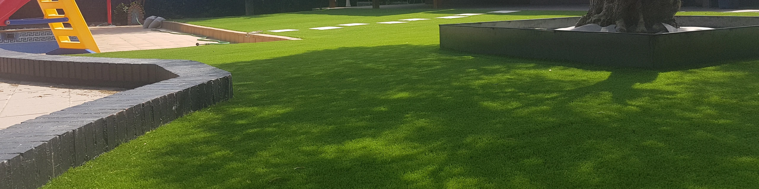 Jardín con césped artificial, árboles y zona de juegos