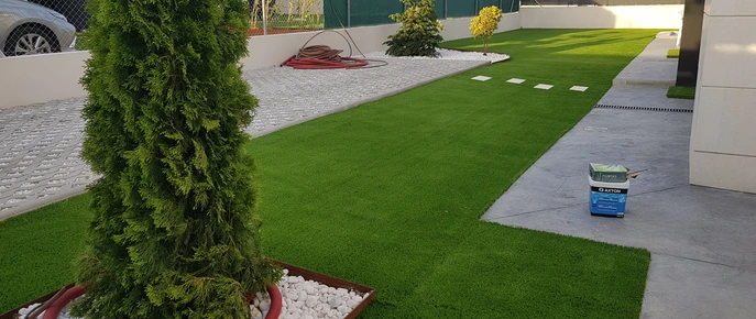 Césped artificial con árbol y perfil delimitando una zona de piedra