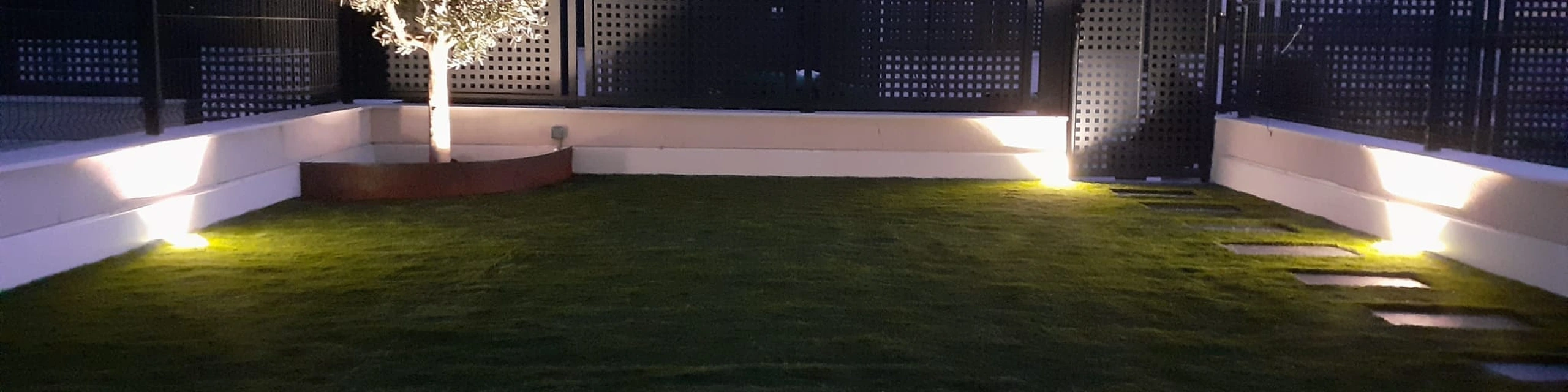 Jardín con césped artificial y luces junto a los muros