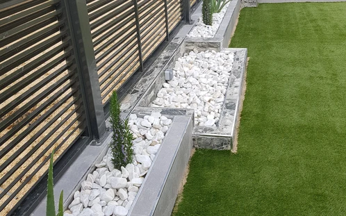 Jardinera de obra con grava blanca junto a una valla