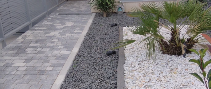 Zona de áridos grises y blancos junto a una palmera y pavimento
