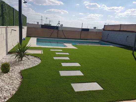 Terraza con césped artificial y pasarela de losas junto a una vivienda