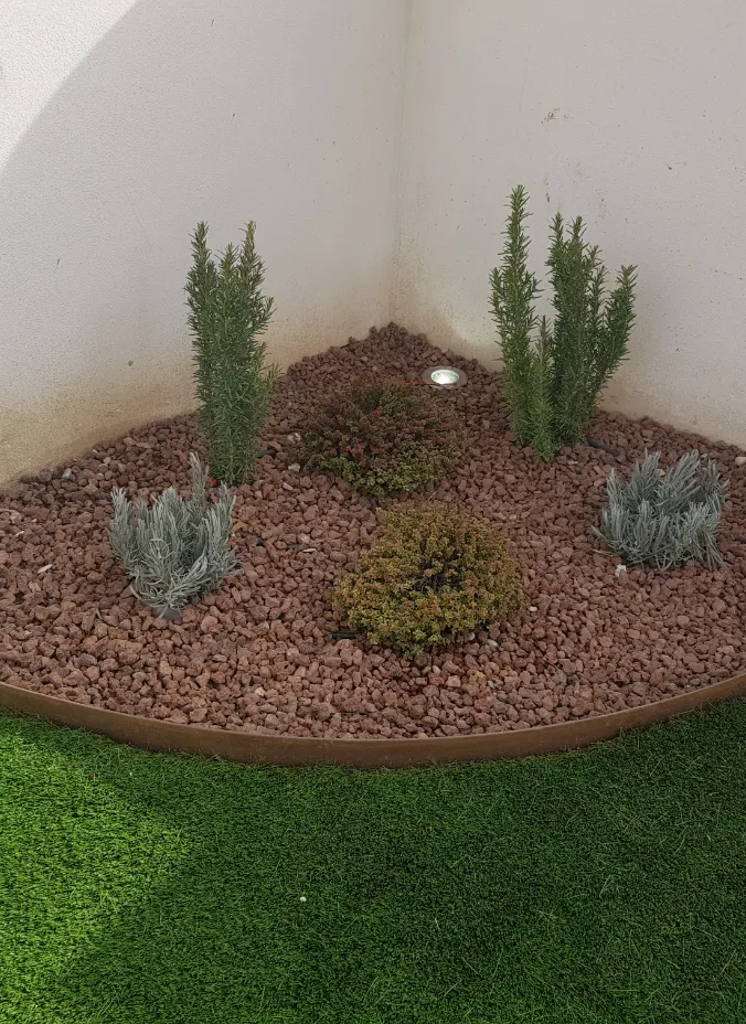 Jardín con césped artificial y plantas junto a una pared